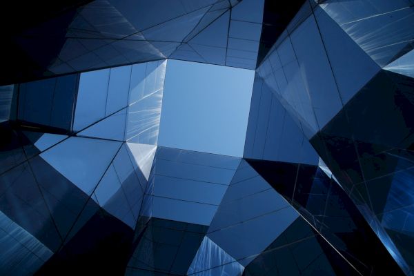 The image shows a geometric pattern of reflective glass panels forming an open, square-shaped skylight, with a view of the sky.