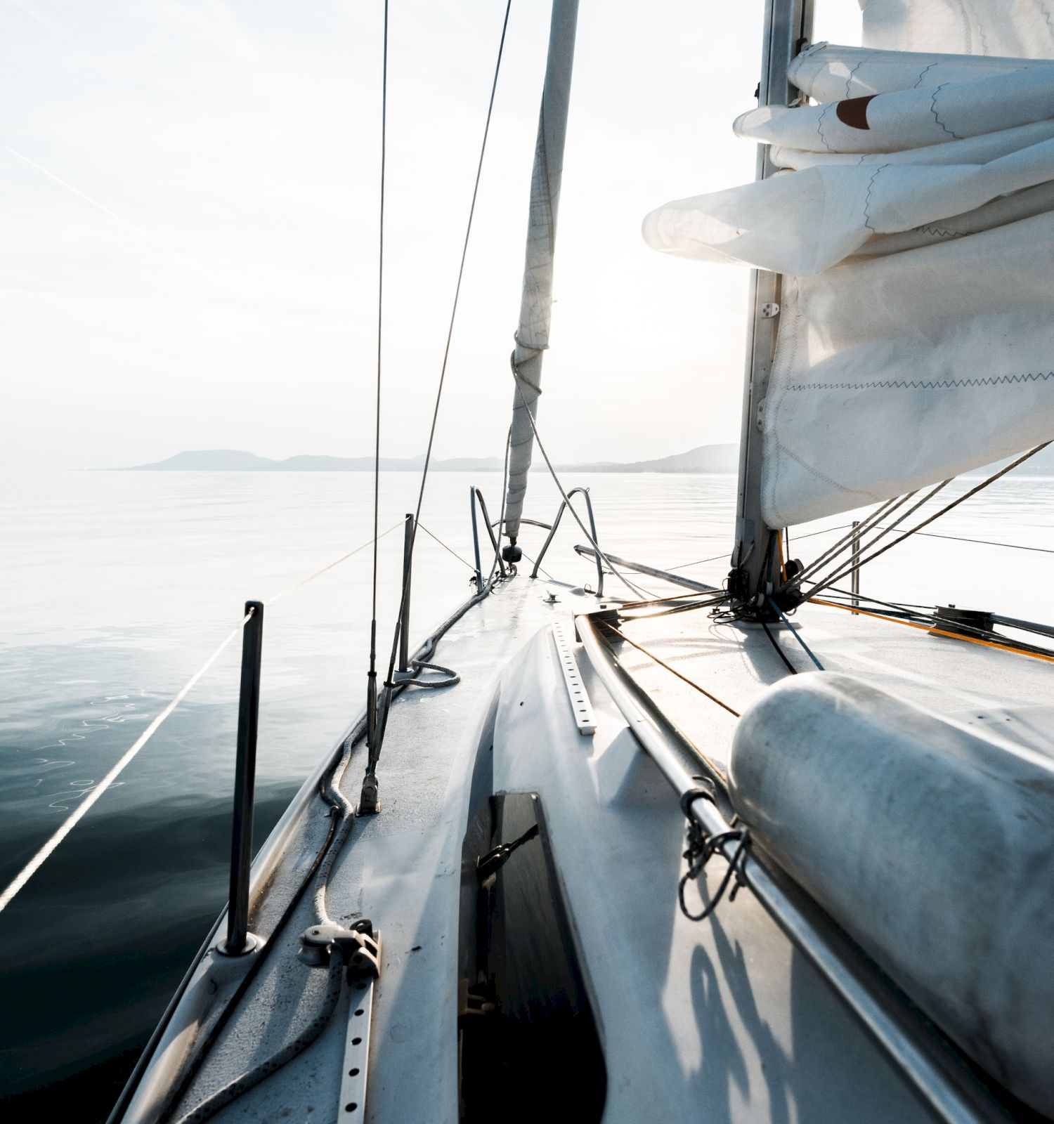 A picturesque view from the deck of a sailboat on a calm sea, with sails billowing and a serene horizon in the background.