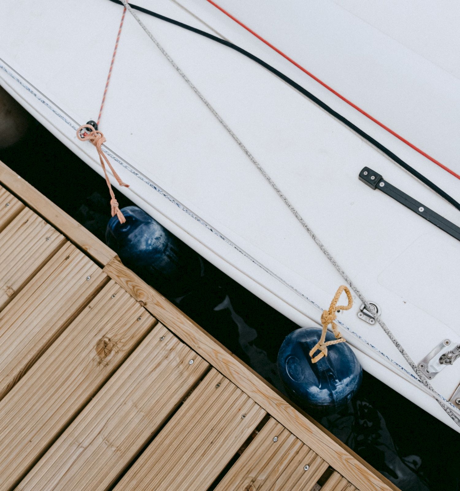 A docked boat with blue fenders is seen next to wooden decking. Ropes are attached to the boat for securing it in place, ensuring stability.