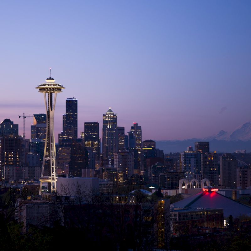 The image depicts the Seattle skyline at dusk, with the Space Needle prominently visible and Mount Rainier in the background.