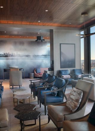 A modern lounge area with ample seating, large windows showcasing a waterfront view, and a wall mural of a city skyline, ending the sentence.