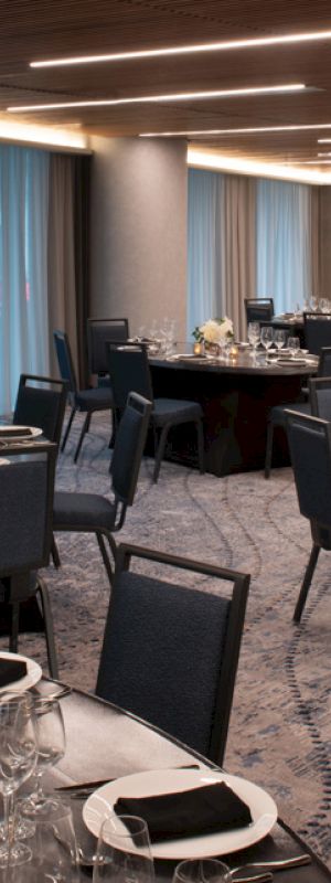 This image shows an elegantly set banquet hall with round tables, black chairs, and place settings. The room has dim lighting and modern decor.